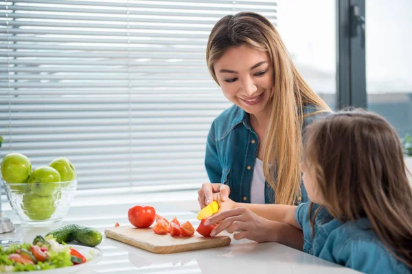 Cheerful mother cutting vegetables together with her child — Stock Photo, Image