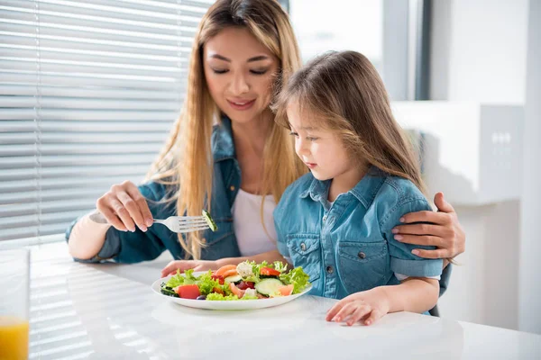 Cheerful woman feeding her little daughter by healthy food — Stock Photo, Image