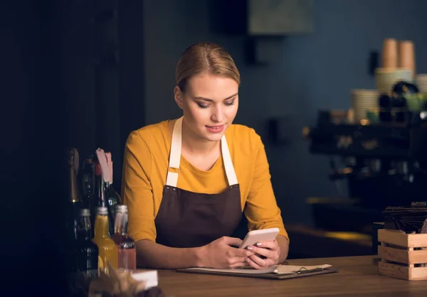 Chica amable escribiendo en el teléfono en el mostrador — Foto de Stock