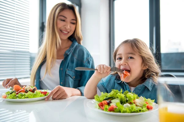 Mãe alegre e filha degustação salada na cozinha Imagem De Stock