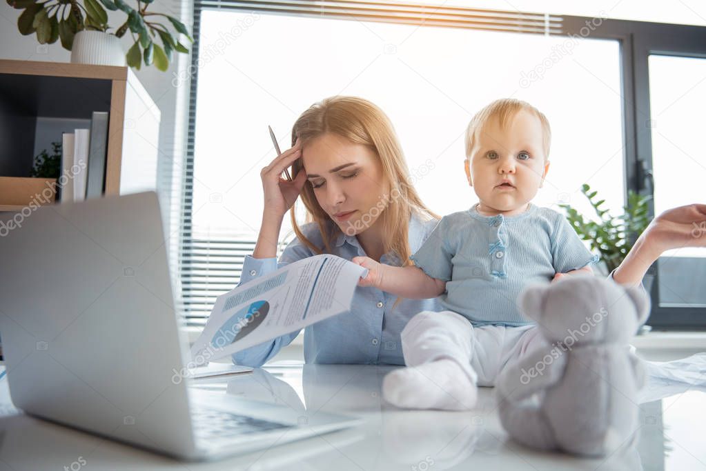 Weary mother working with baby in office