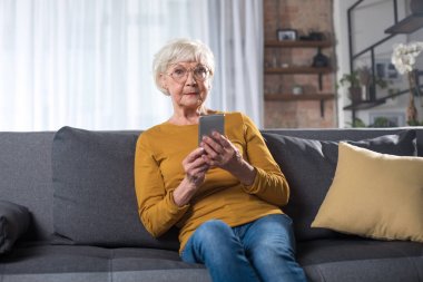 Telefon ile oturma odasında kanepede oturan yaşlı kadını etkiledi