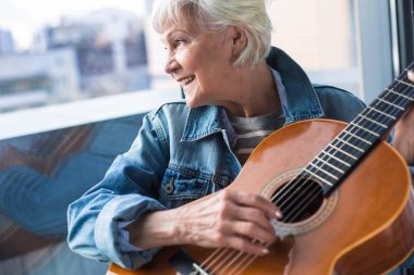 Zarif yaşlı kadın müzik aleti pencerede otururken holding