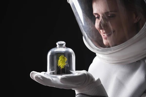 Счастливая леди астронавт с интересом смотрит на зеленое растение — стоковое фото