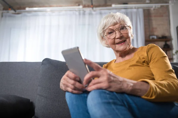 Цікава розумна старенька розслабляється вдома з мобільним пристроєм — стокове фото