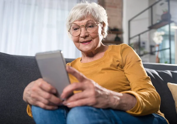 Mujer jubilada sonriente interesada mirando el teléfono celular en casa — Foto de Stock