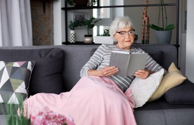 Yaşlı dalgın Bayan kitap ile kanepede rahatlatıcı