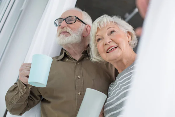 Upphetsad gifta äldre pensionärer tittar över fönster med te — Stockfoto