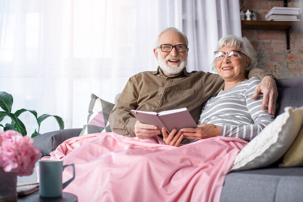 Excited senior husband and wife with book at living room