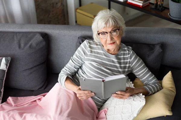 Nachdenkliche Dame liest Buch im Wohnzimmer — Stockfoto