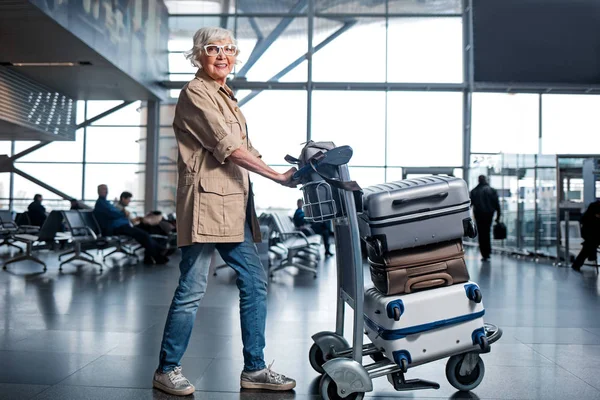 Optimiste dame âgée passe par la salle d'attente avec des bagages — Photo