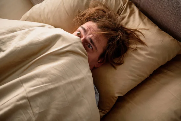 Un hombre asustado que no quiere levantarse por la mañana. —  Fotos de Stock