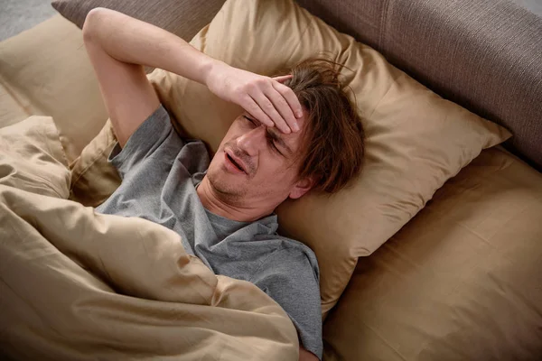 Уставший парень, страдающий мигренью в спальне — стоковое фото