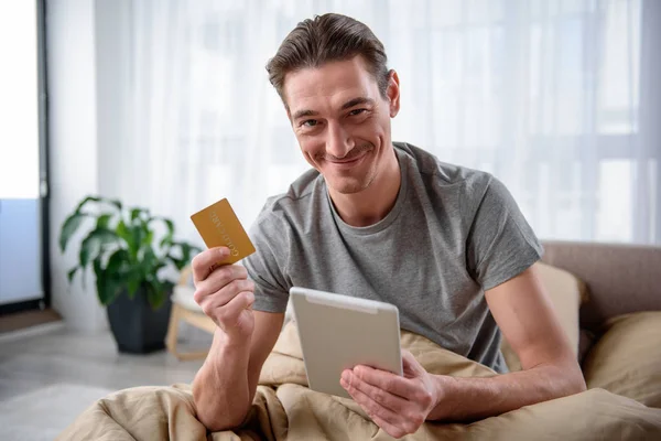 Homem Contentado mostrando dispositivo moderno e cartão de ouro — Fotografia de Stock