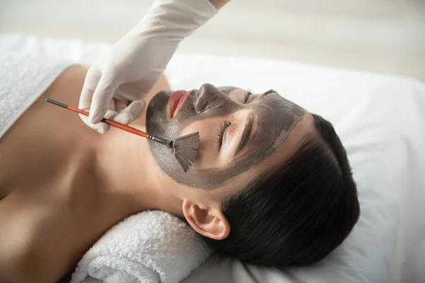 Esteticista fazendo máscara facial para mulher jovem — Fotografia de Stock