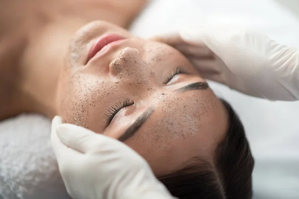 Esteticista aplicando esfoliação no rosto feminino — Fotografia de Stock
