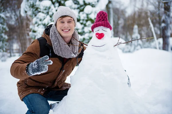 Веселый парень, стоящий рядом с фигурой из снега зимой — стоковое фото