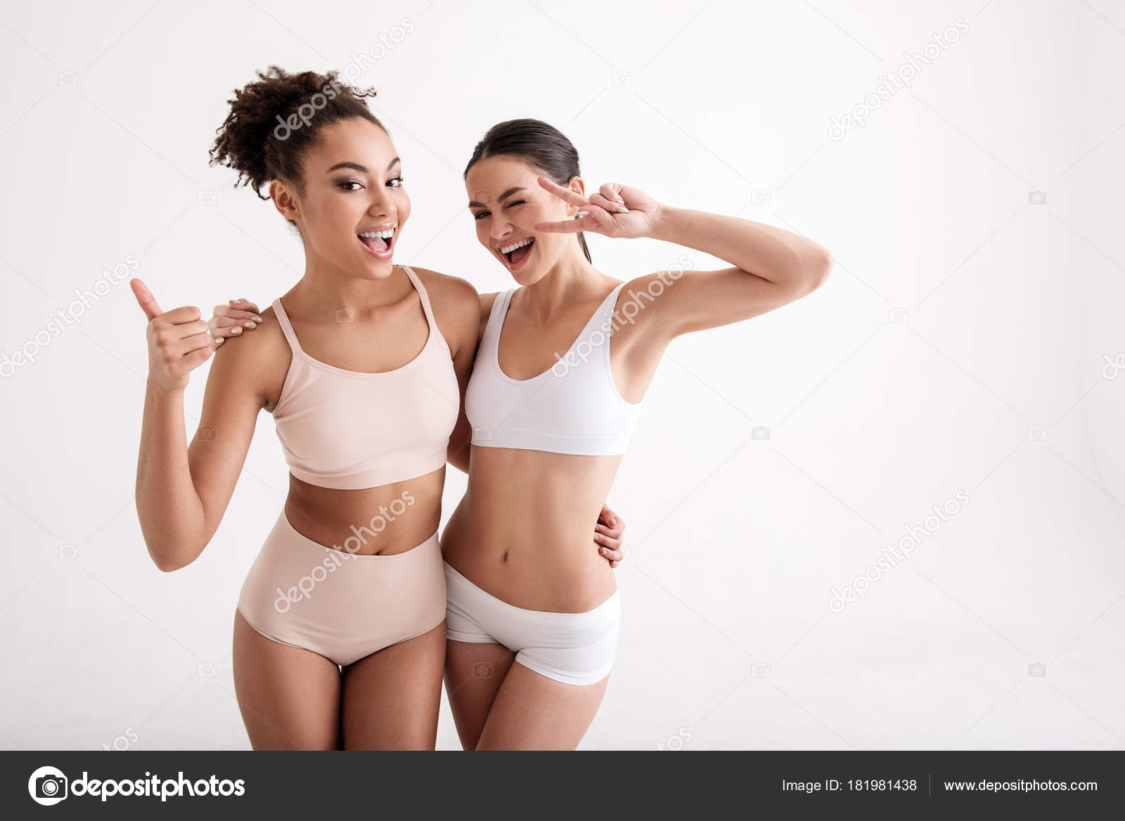 Portrait of two smiling women in great shape wearing tight underwear. They  are hugging and looking at camera with joy. Copy space in right side.  Isolated on background Photos