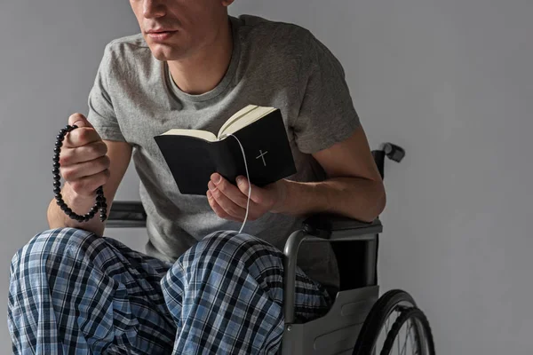 Орієнтована людина в інвалідному візку тримає Біблію і розарій — стокове фото