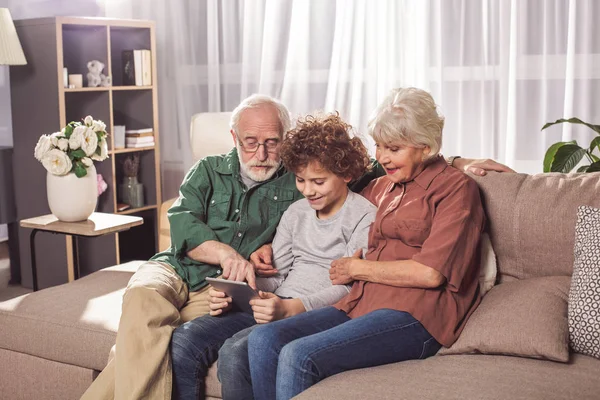 Gelukkig gepensioneerden met kleinzoon kijken naar gadget — Stockfoto