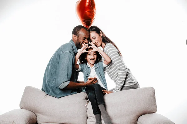Зміст дівчина демонструє знак любові, а сім'я відпочиває на дивані — стокове фото