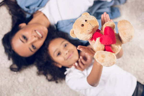 Mãe feliz e criança descansando no tapete com ursinho de pelúcia — Fotografia de Stock