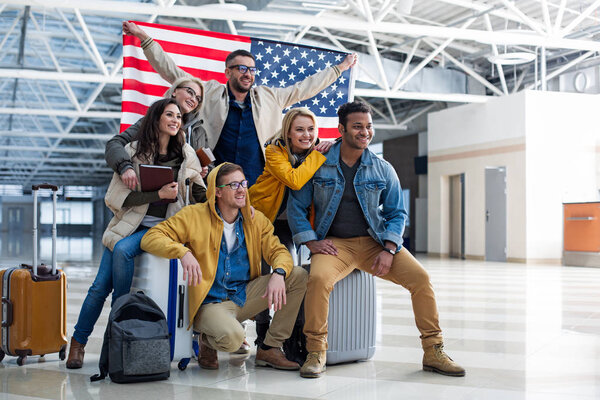 Cheerful company of friends standing with banner at the airport