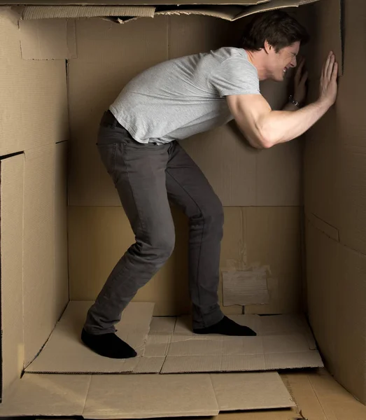 Guy está expresando irritación mientras está dentro de una pequeña sala de cartón — Foto de Stock