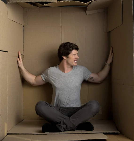 Hombre joven está presionando en las paredes dentro de la caja de cartón — Foto de Stock