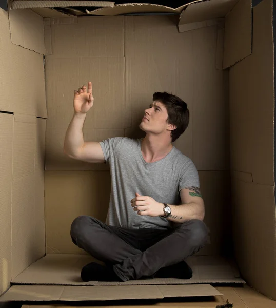 Guy está posando dentro de una pequeña sala de cartón y esperando algo — Foto de Stock