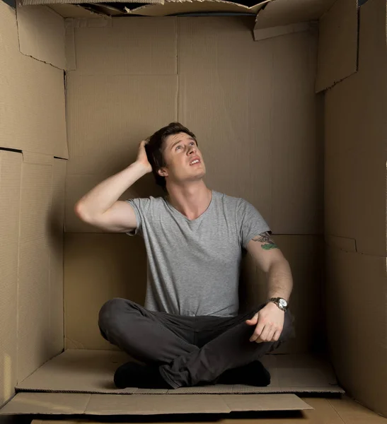 Anxious guy is sitting in cardboard room — Stock Photo, Image