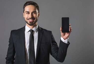 Smiling handsome businessman showing modern smartphone clipart