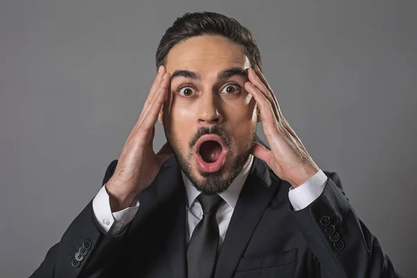 Young shocked businessman opening mouth and clutching head — Stock Photo, Image