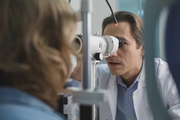 Focused ophthalmologist checking eyes of client — Stock Photo, Image