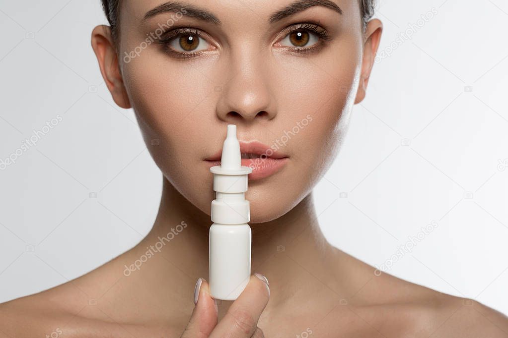Serene young woman treating her runny nose by spray