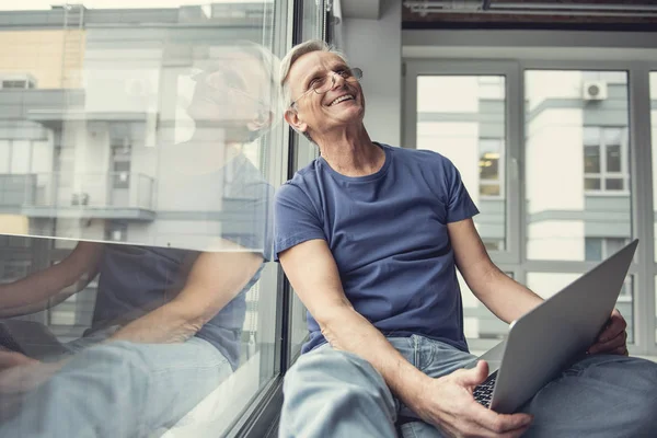 Lycklig äldre man sitter med gadgeten på knän — Stockfoto