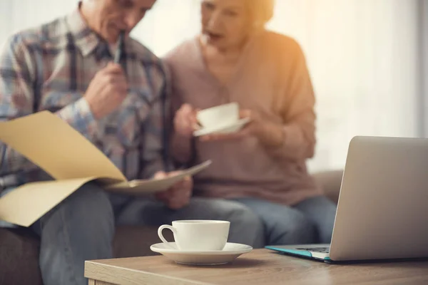 Cup och anteckningsboken på skrivbord nära senior pensionärer — Stockfoto