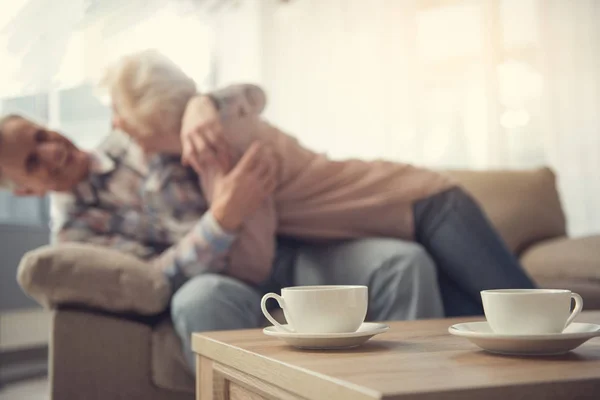 Dos tazas en la mesa de madera cerca de pareja madura — Foto de Stock