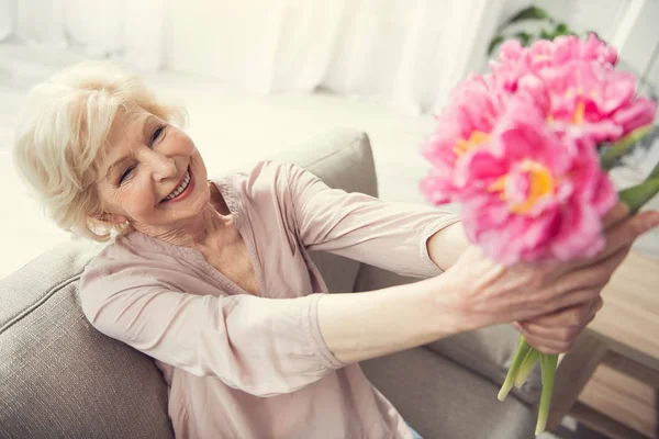 Alte fröhliche Frau sitzt mit Blumen — Stockfoto