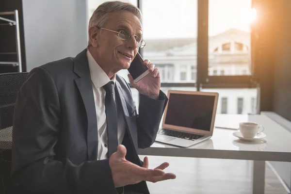 Cheerful retire talking by mobile during work