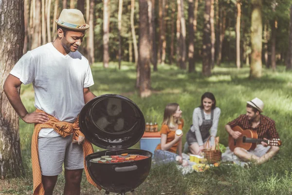 Радостный человек готовит барбекю для друзей в лесу — стоковое фото