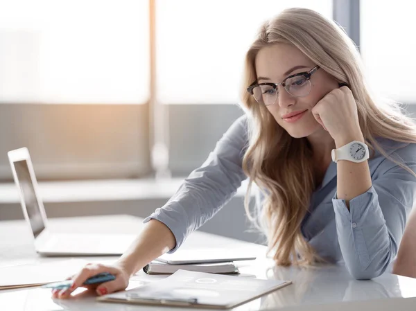 Fröhliche blonde Frau analysiert Papiere am Arbeitsplatz — Stockfoto