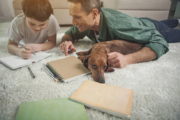 Hombre alegre ayudando al niño a hacer la tarea cerca de la mascota — Foto de Stock