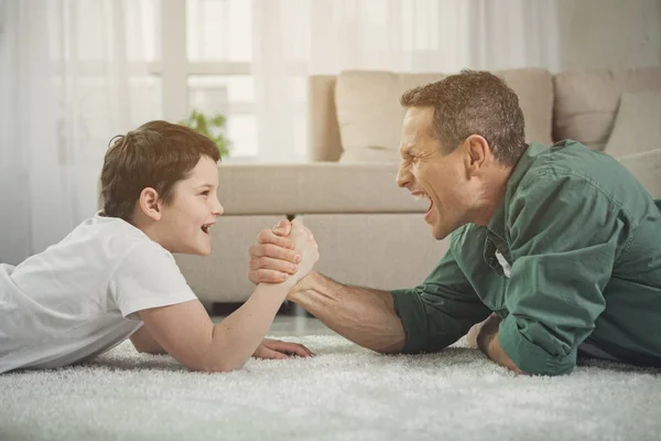 Cheerful father and son playing arm-wrestling at home — Stock Photo, Image