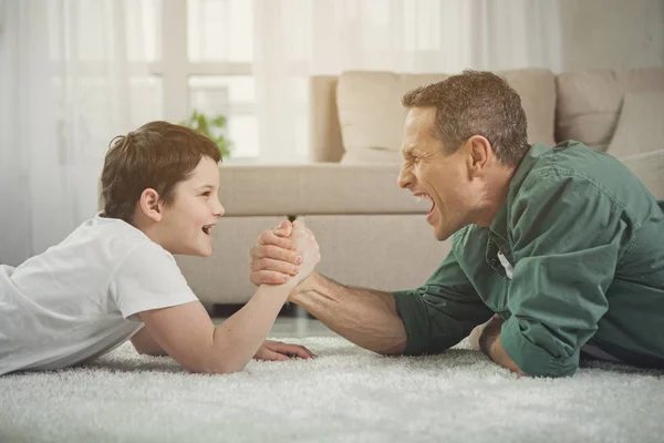 Alegre pai e filho jogando braço-de-ferro em casa — Fotografia de Stock