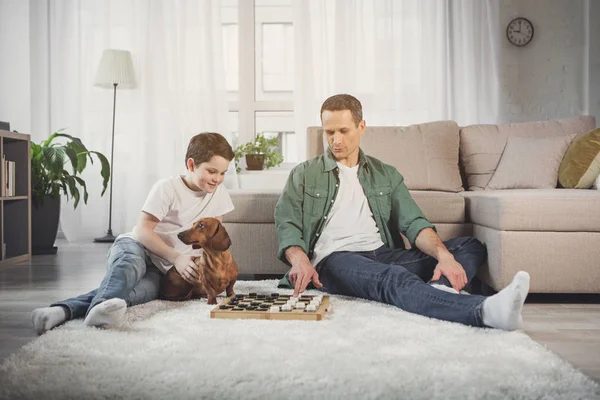 Munter far og dreng spiller dam derhjemme - Stock-foto