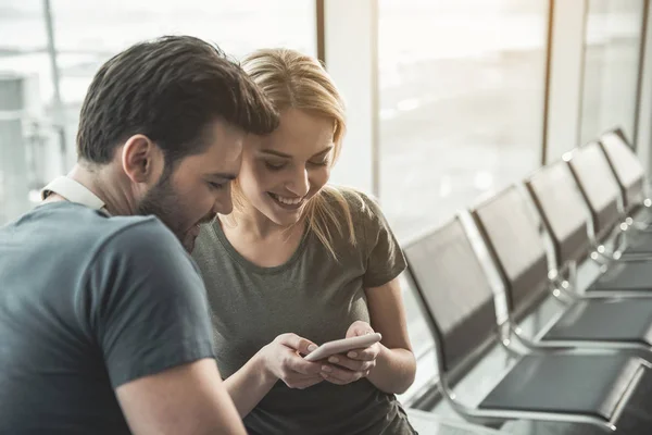 Beaming lovers looking at mobile in hall — Stock Photo, Image