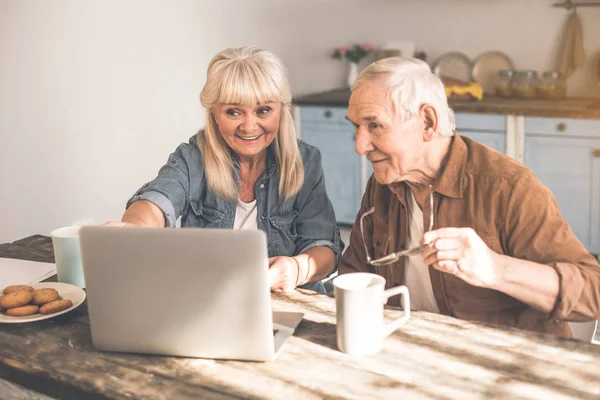 Alegre pareja de ancianos casados utilizando la computadora en la sala de cocina — Foto de Stock