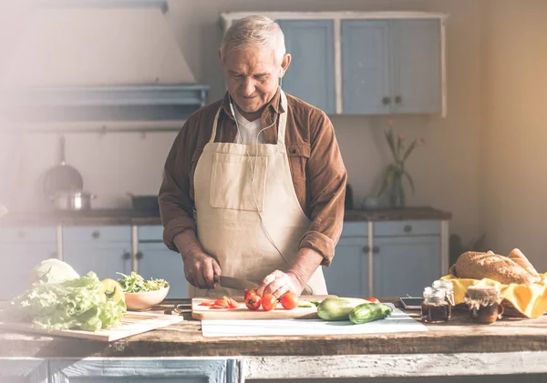 Rustig volwassen houseman snijden van groenten en genieten van nummer — Stockfoto