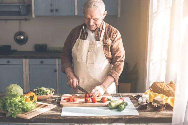 Fröhlicher Rentner schneidet Gemüse in Küche — Stockfoto